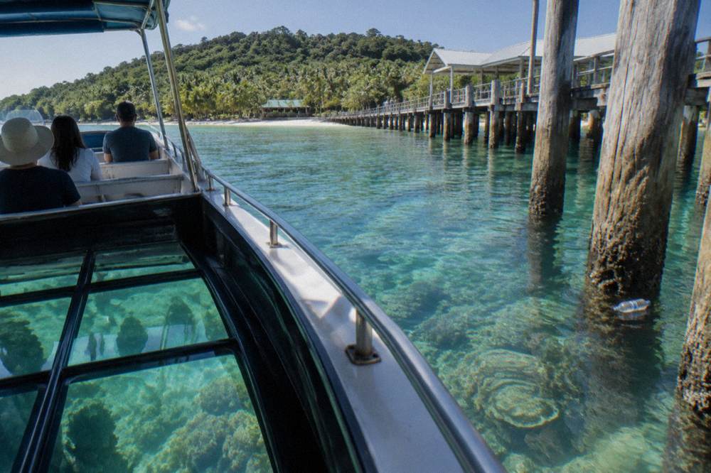 A glass-bottom boat drifting over coral reef in clear shallow water beside an island jetty
